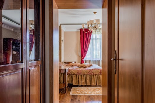 Vue d'une chambre élégante au Château de Sainte-Julie, avec des rideaux rouges et un lustre, à travers une porte en bois.