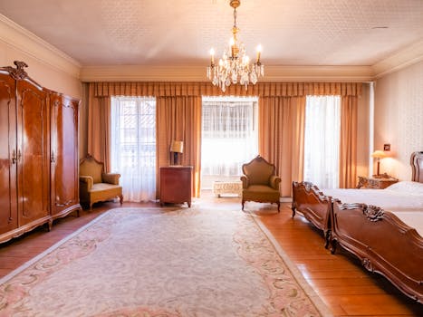 Chambre élégante au Château de Sainte-Julie avec mobilier ancien, lustre et fenêtres drapées.